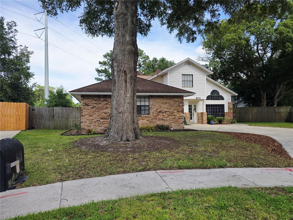 A two-story house with a brick and siding exterior stands behind a large front tree — 8433 COMMANDER COVE, WINTER PARK, FL