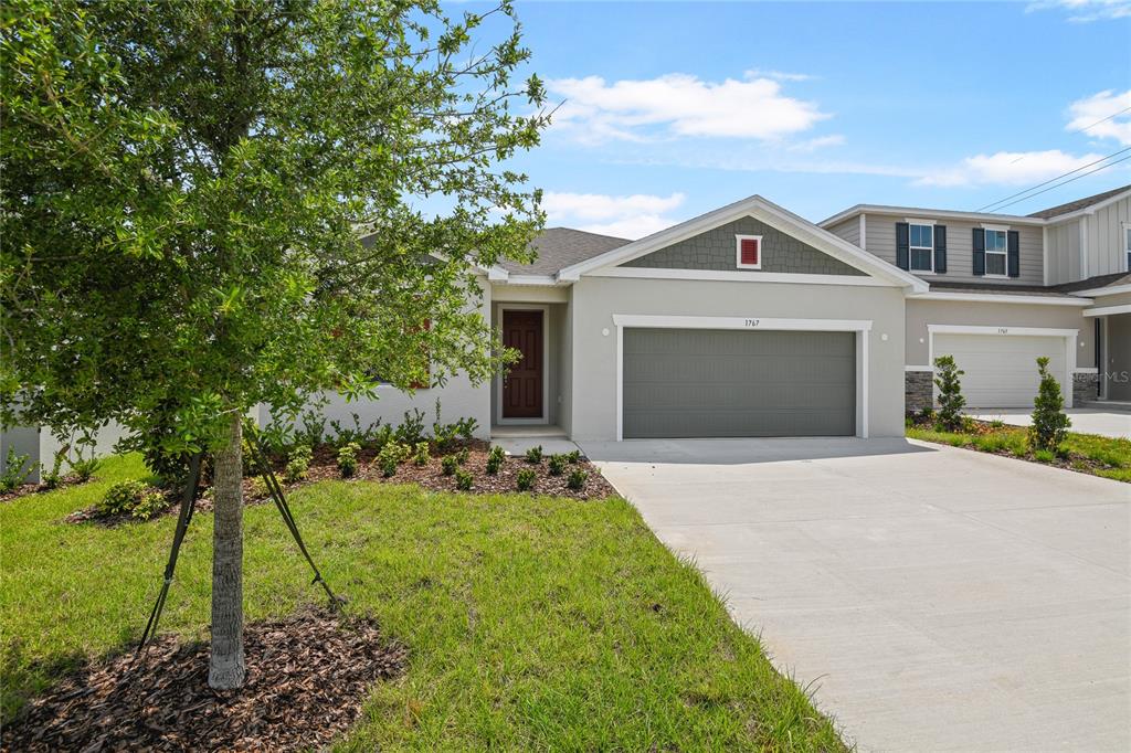 A single-story house with a gray garage, beige stucco exterior, and a front lawn — 1767 CARNELIAN STREET, DELAND, FL
