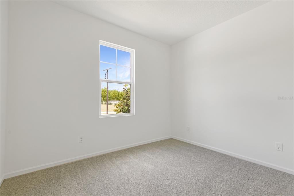 An empty bedroom features white walls, gray carpet, and a single window with exterior views — 1767 CARNELIAN STREET, DELAND, FL