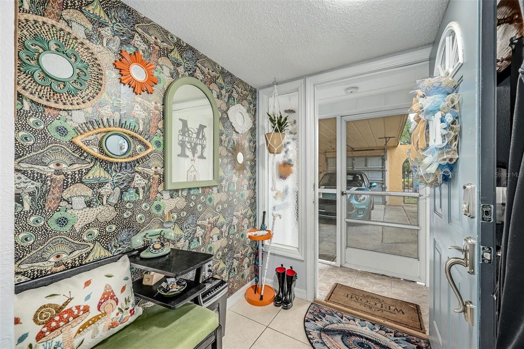 An entryway features mushroom-patterned wallpaper, a green bench, a vintage phone, and a screen door — 3546 DAIRY ROAD, TITUSVILLE, FL