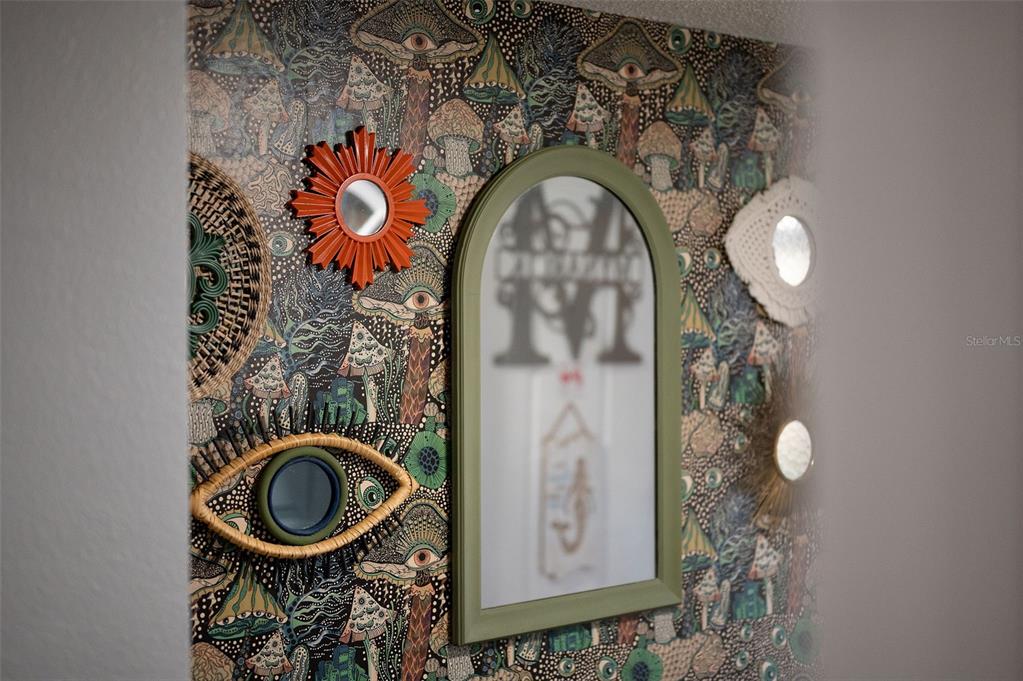 An arched mirror hangs on a wall covered in mushroom-patterned wallpaper with several decorative mirrors — 3546 DAIRY ROAD, TITUSVILLE, FL