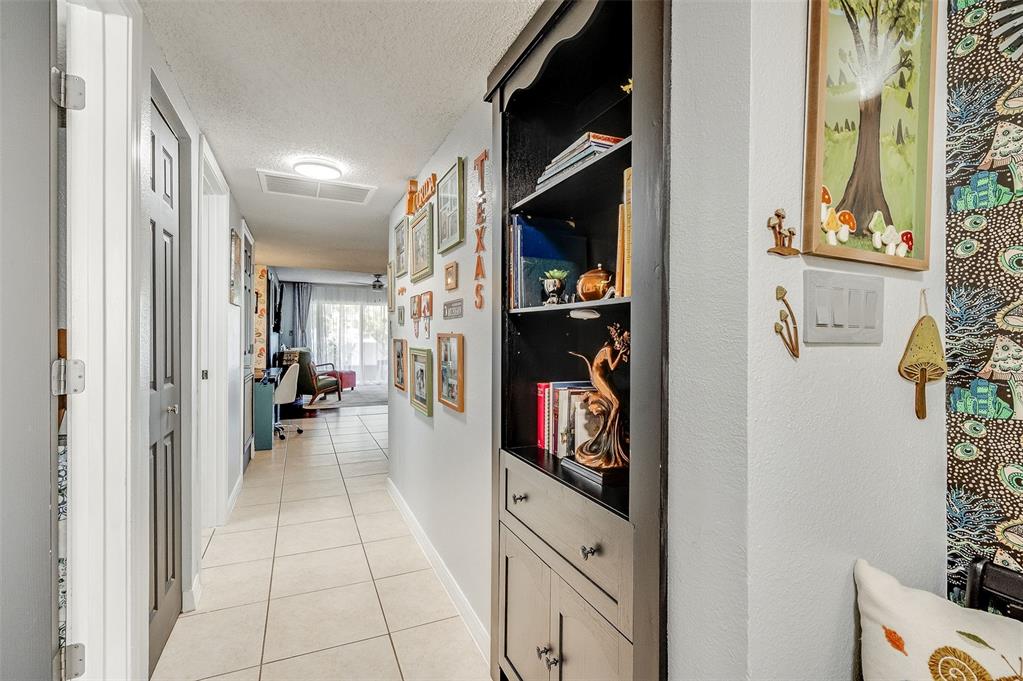 A hallway with tiled floors leads to a living area past a tall black bookshelf — 3546 DAIRY ROAD, TITUSVILLE, FL