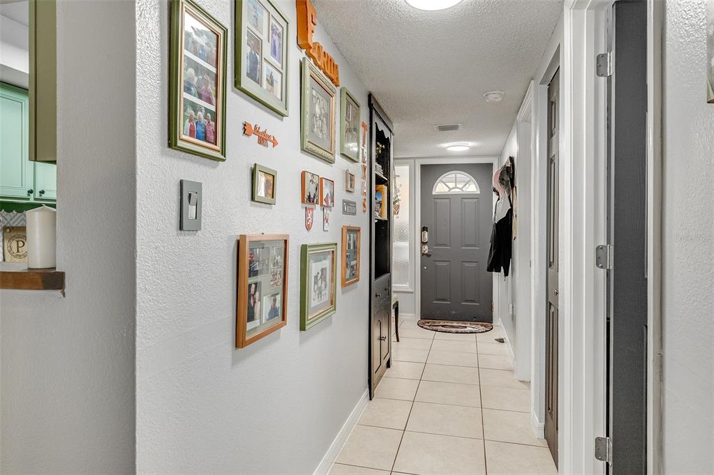 A hallway with tiled floors, a gallery wall of photos, and a dark front door — 3546 DAIRY ROAD, TITUSVILLE, FL
