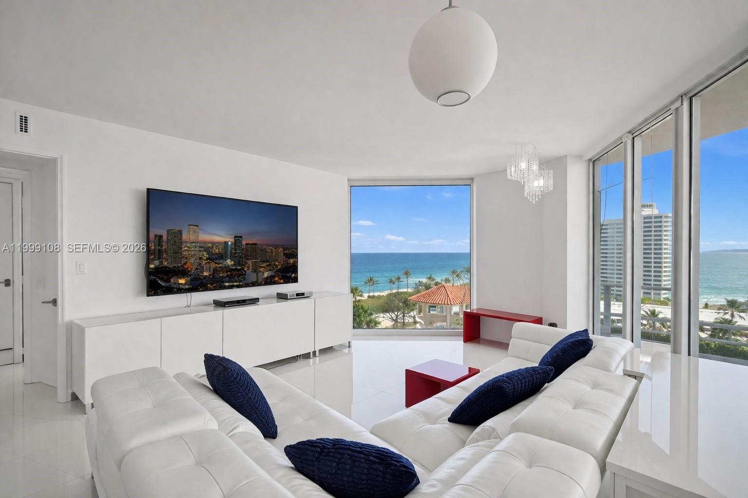 A modern white living room features a large sectional sofa, wall-mounted television, and ocean views — 7330 Ocean Ter # C, Miami Beach FL 33141, MIAMI BEACH, FL