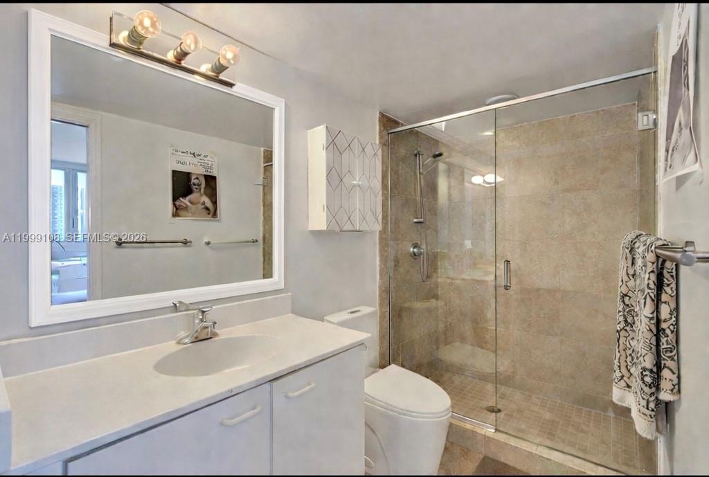 A bathroom featuring a white vanity, a large mirror, a toilet, and a glass-enclosed shower — 7330 Ocean Ter # C, Miami Beach FL 33141, MIAMI BEACH, FL