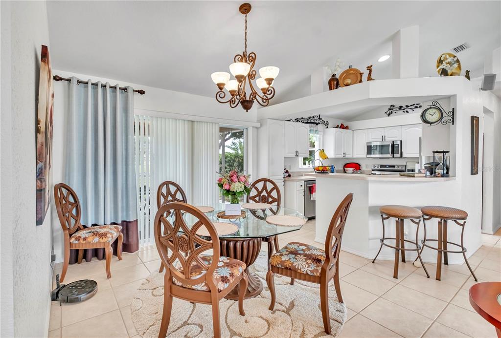 A dining area with a glass table, patterned chairs, and an adjacent kitchen with white cabinets — 7360 N FICUS TREE, PUNTA GORDA, FL
