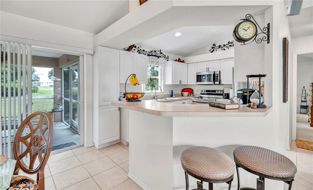 A kitchen features white cabinets, a breakfast bar with two stools, and a sliding glass door — 7360 N FICUS TREE, PUNTA GORDA, FL