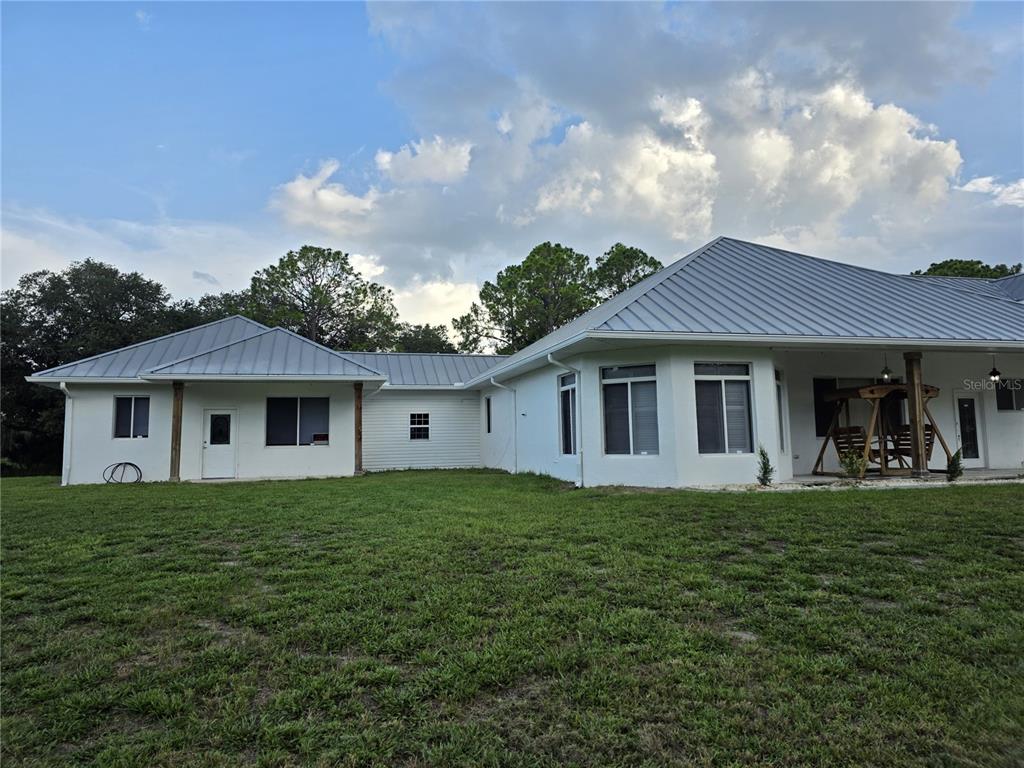 The exterior of a white house with a metal roof and a grassy backyard — 837 LILY STREET, SEBRING, FL