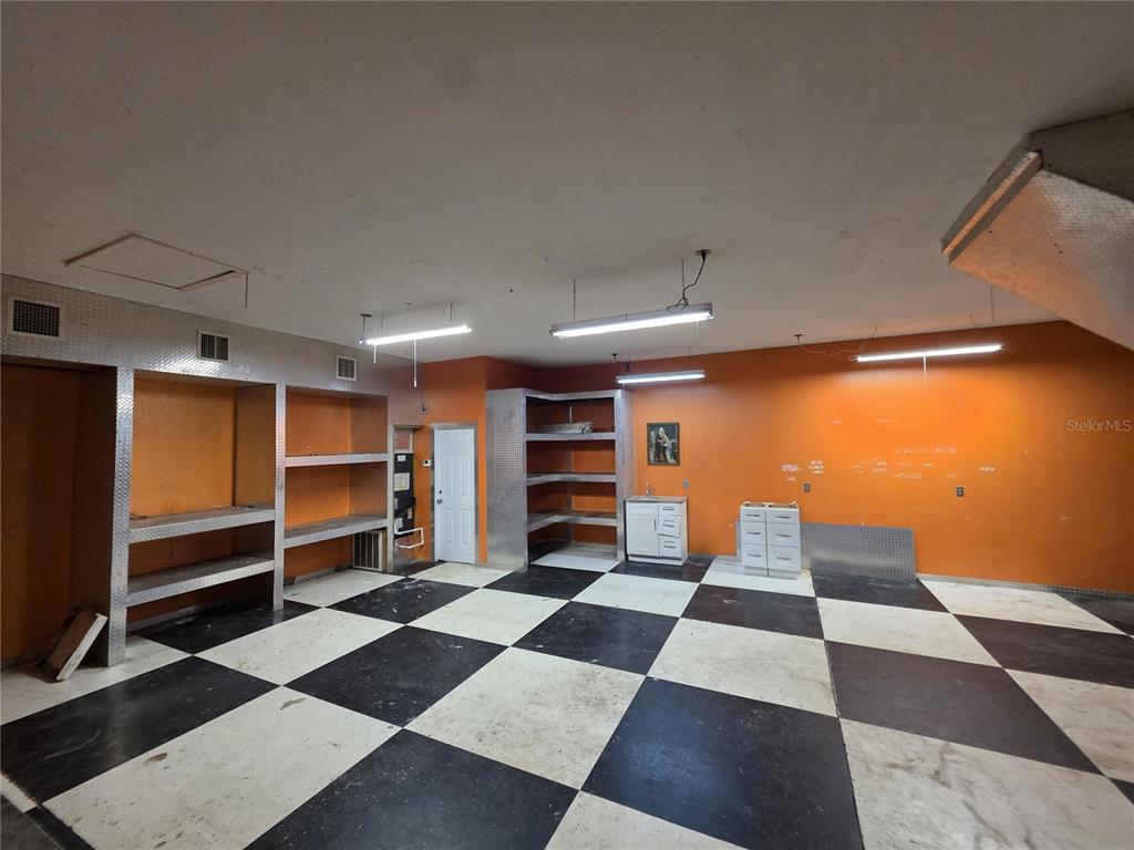 A garage with orange walls, checkerboard flooring, built-in metal shelving, and fluorescent lighting — 837 LILY STREET, SEBRING, FL