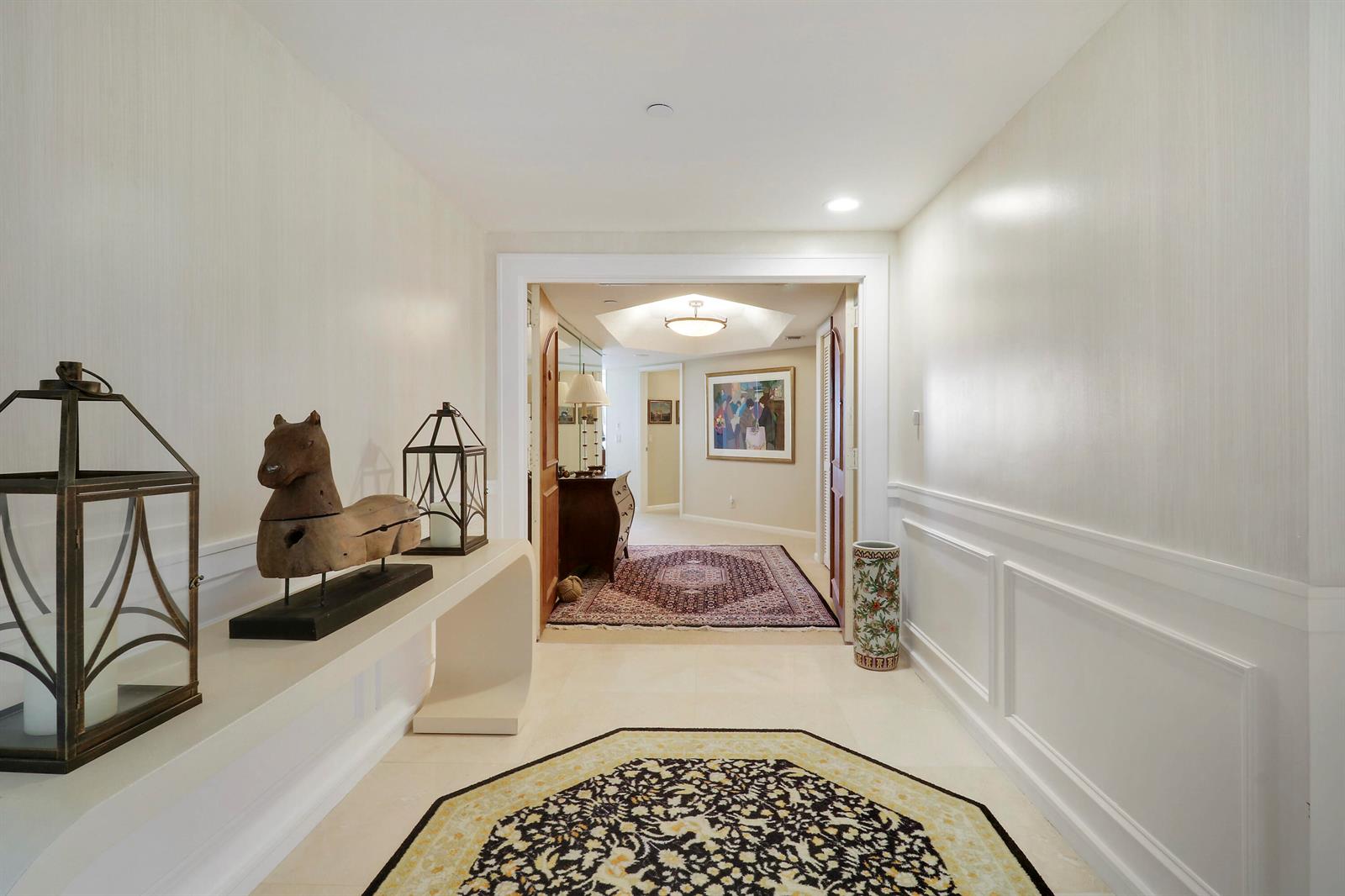 A hallway with a console table, horse sculpture, and lanterns leads into a carpeted room — 3322 Casseekey Island Road # 604, Jupiter FL 33477, JUPITER, FL