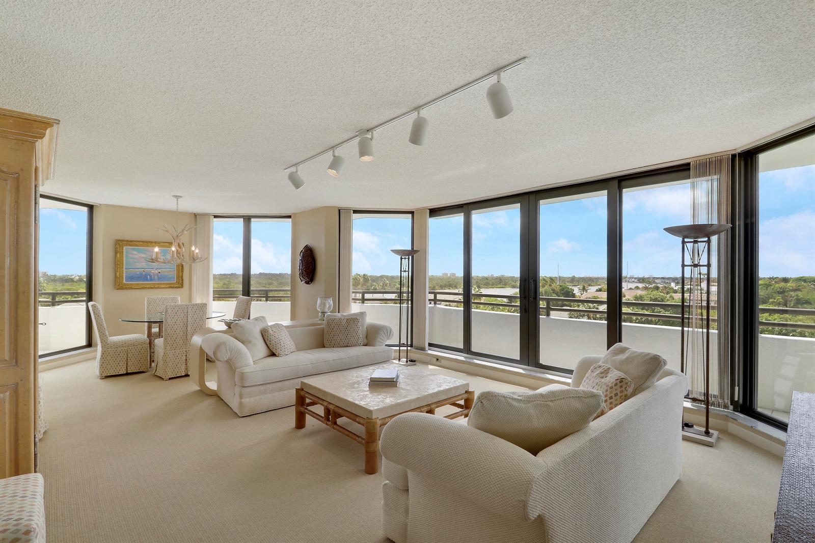A living and dining area with beige carpet, white furniture, and floor-to-ceiling windows overlooking greenery — 3322 Casseekey Island Road # 604, Jupiter FL 33477, JUPITER, FL
