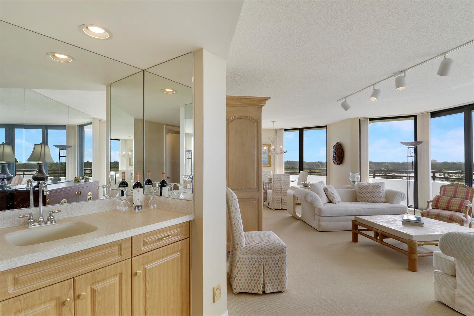 A wet bar with light wood cabinets and a mirror overlooks a bright living area — 3322 Casseekey Island Road # 604, Jupiter FL 33477, JUPITER, FL