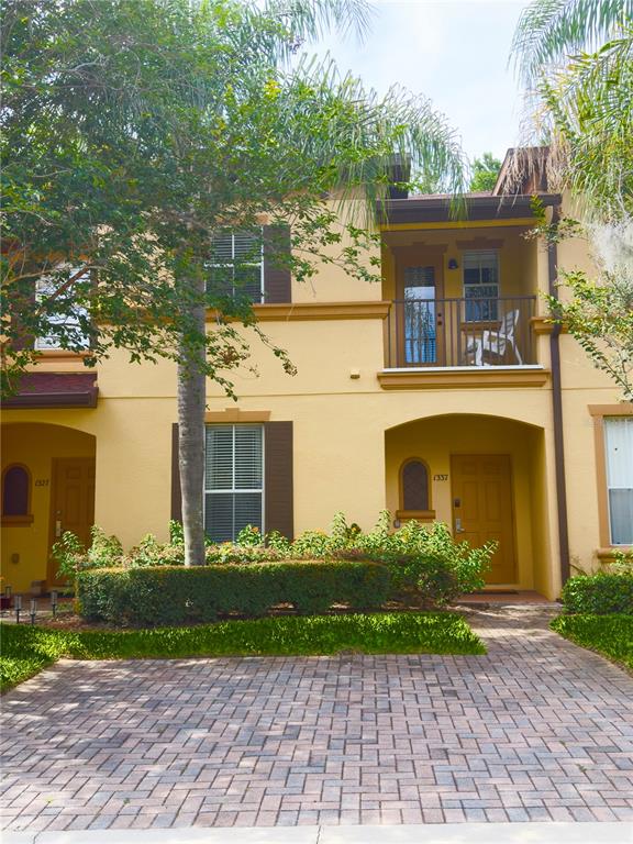 A two-story yellow stucco townhouse with a brick paver driveway and a second-floor balcony — 1337 CALABRIA AVENUE, DAVENPORT, FL