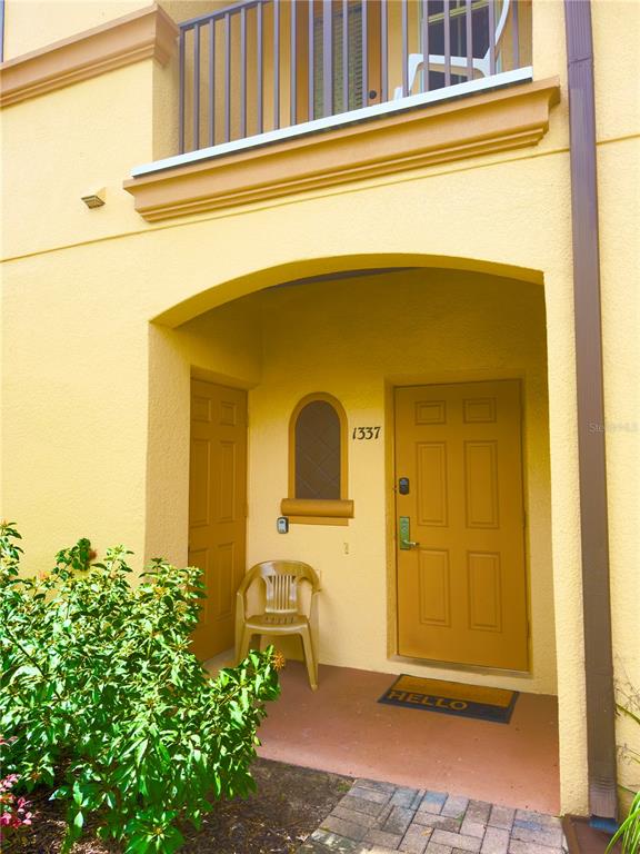 The exterior entrance of a yellow building features a door numbered 1337 and a chair — 1337 CALABRIA AVENUE, DAVENPORT, FL