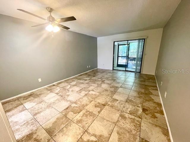 An empty room features light-colored tile flooring, a ceiling fan, and a sliding glass door — 2780 PARK DRIVE UNIT C-3, CLEARWATER, FL
