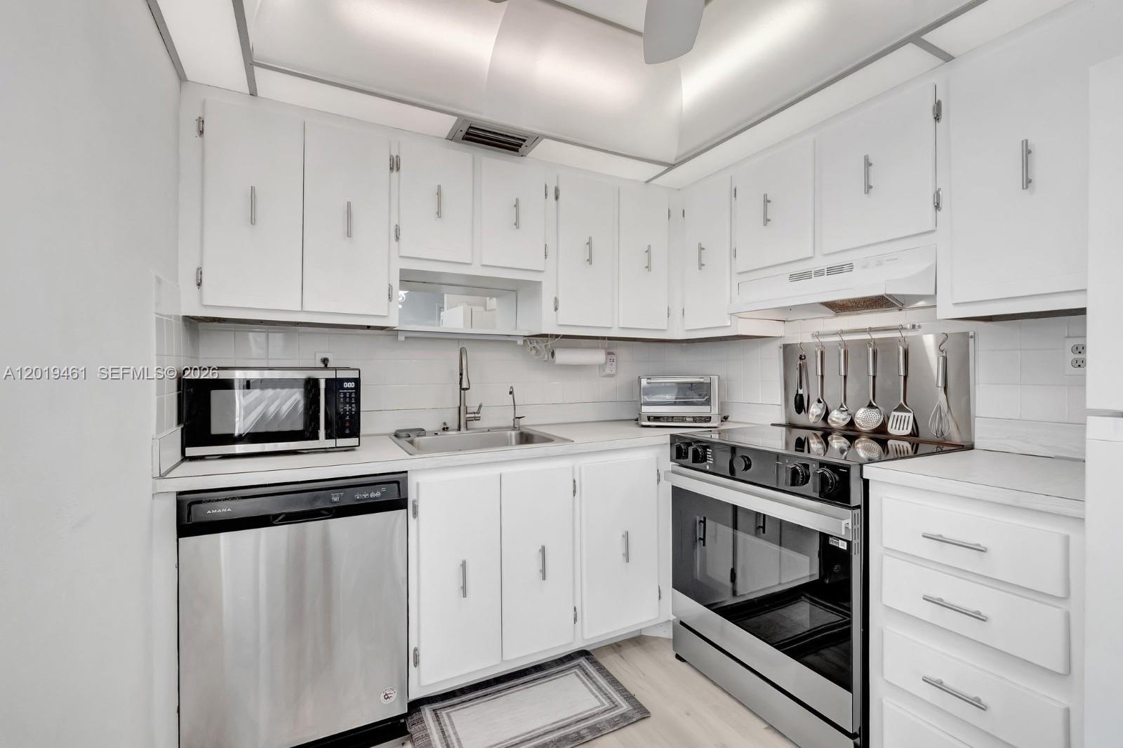 A kitchen features white cabinets, stainless steel appliances, and a tiled backsplash — 481 Burgundy K # K, Delray Beach FL 33484, DELRAY BEACH, FL