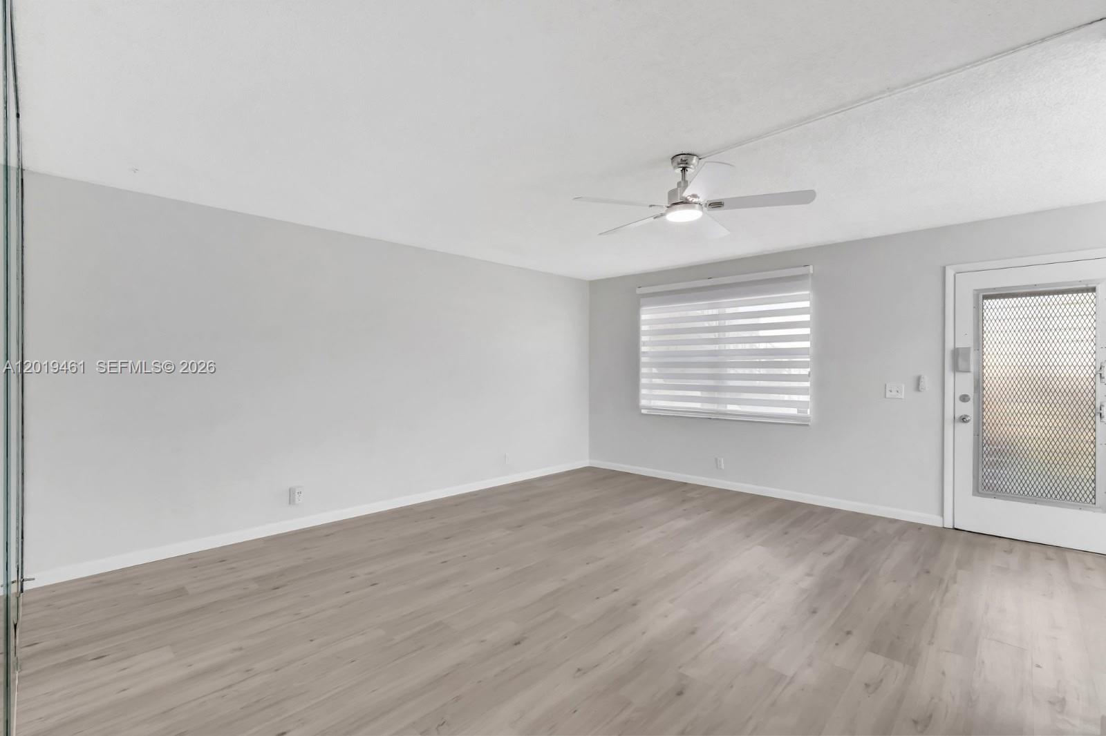 An empty room features light gray walls, wood-look flooring, a ceiling fan, and a door — 481 Burgundy K # K, Delray Beach FL 33484, DELRAY BEACH, FL