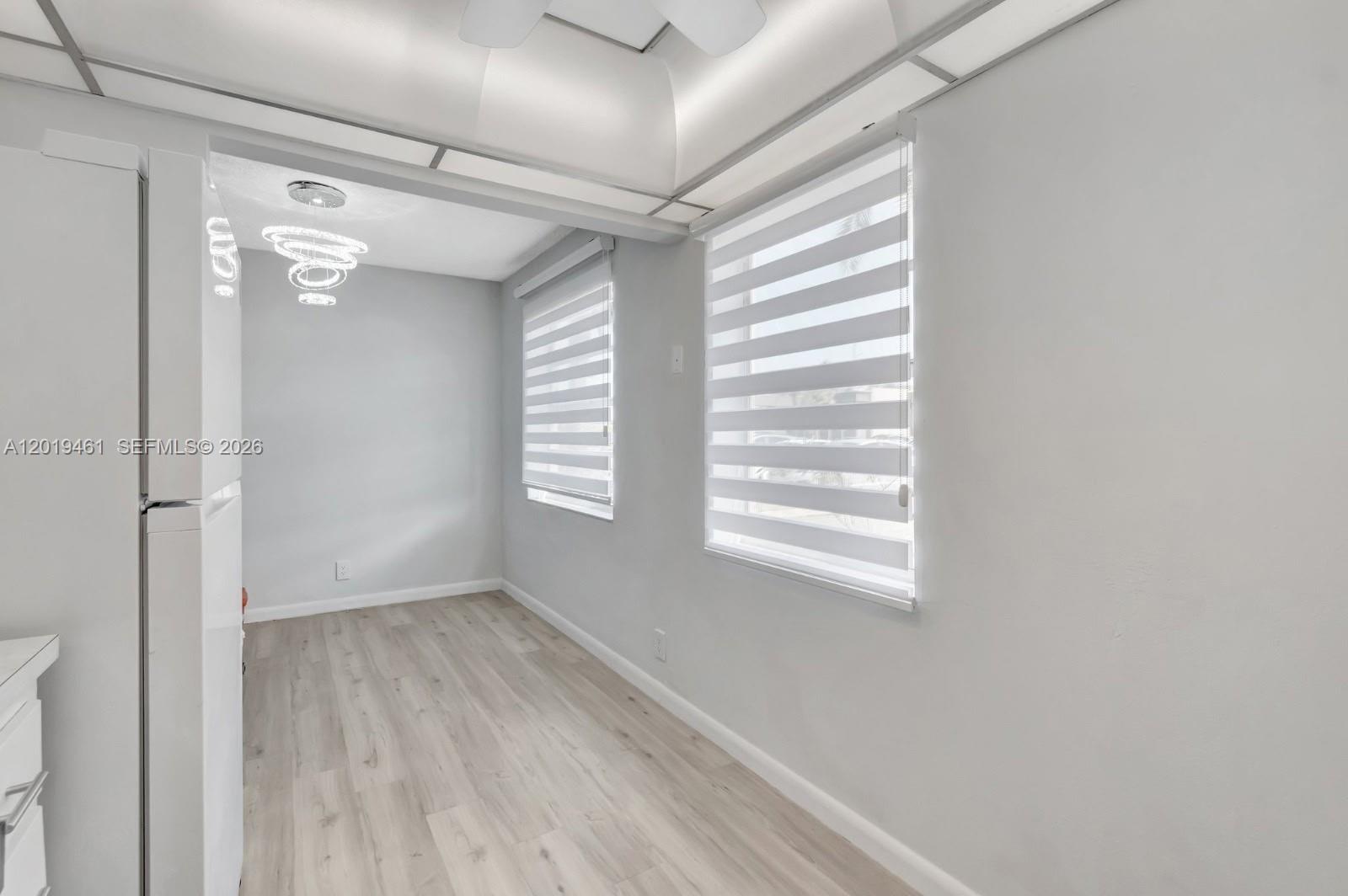 A bright, empty room features light wood-look flooring, gray walls, and two striped window shades — 481 Burgundy K # K, Delray Beach FL 33484, DELRAY BEACH, FL