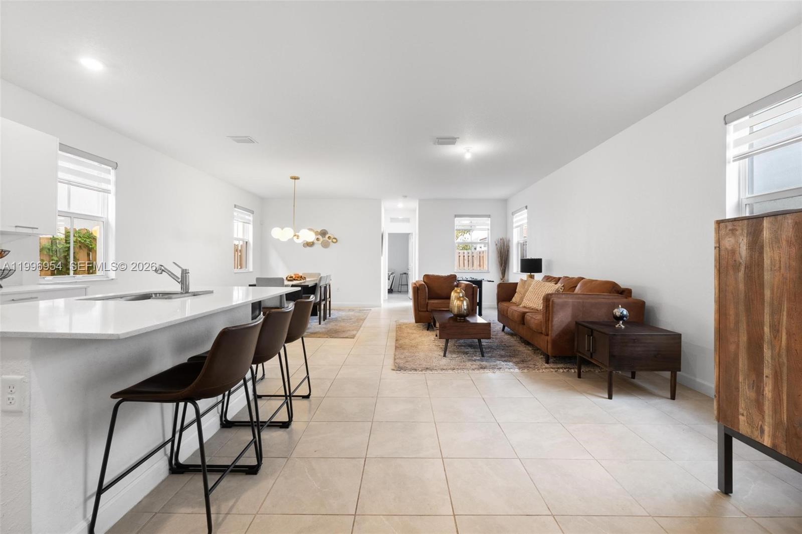 An open-concept living and dining area features a kitchen island with bar stools and tile flooring — 2357 NW 130th St, Miami FL 33167, MIAMI, FL