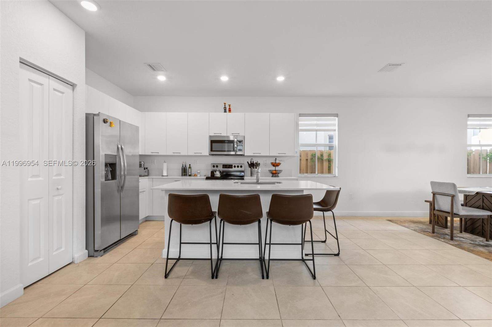 A modern kitchen features white cabinetry, stainless steel appliances, and a central island with stools — 2357 NW 130th St, Miami FL 33167, MIAMI, FL