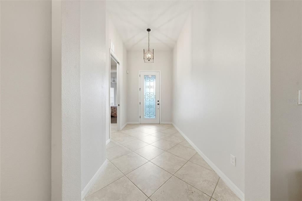 A bright entryway features light-colored tile flooring, white walls, and a decorative glass front door — 30040 DONNINGTON LOOP, MOUNT DORA, FL