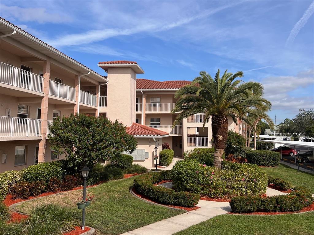 A multi-story apartment building with a palm tree and landscaped courtyard in the foreground — 6501 STONE RIVER ROAD UNIT 203, BRADENTON, FL