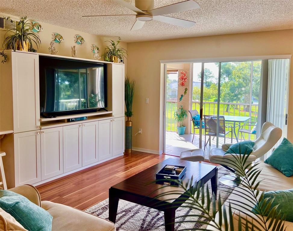 A living room features a large entertainment center, wood flooring, and a sliding glass door — 6501 STONE RIVER ROAD UNIT 203, BRADENTON, FL