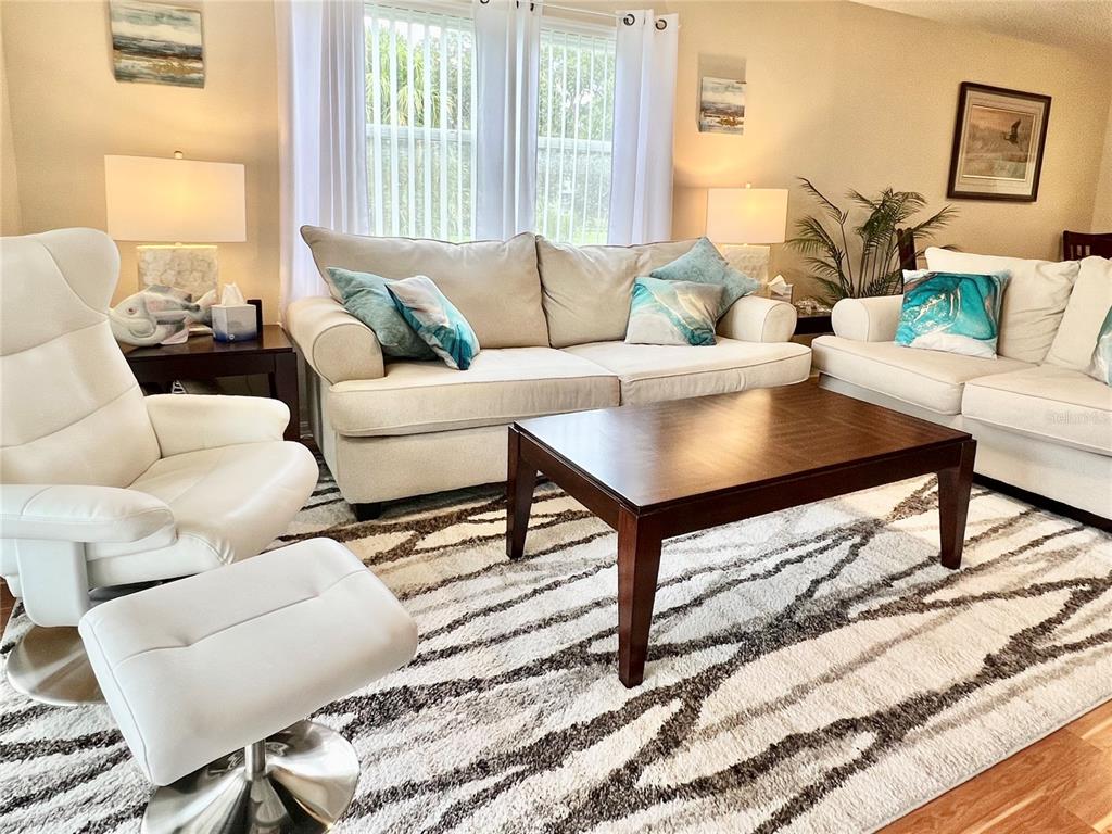 A living room features a white armchair with ottoman, two beige sofas, and a coffee table — 6501 STONE RIVER ROAD UNIT 203, BRADENTON, FL
