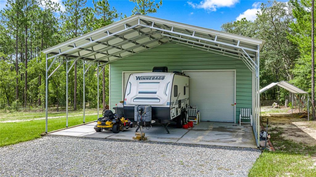 A metal carport shelters a travel trailer, a lawn mower, and a closed garage door — 13130 SW 88TH STREET, DUNNELLON, FL