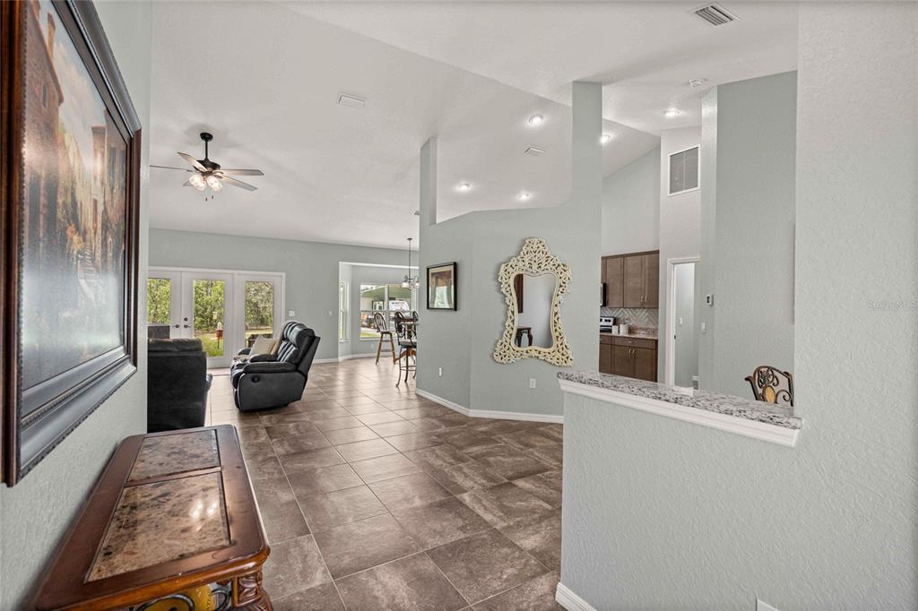 An open-concept living area features tile flooring, light blue walls, and a view into the kitchen — 13130 SW 88TH STREET, DUNNELLON, FL