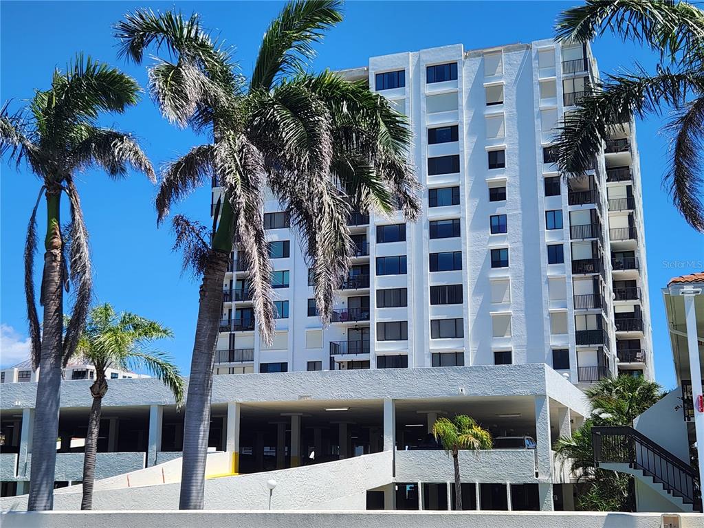 A multi-story white residential building stands behind a parking garage with palm trees in front — 6287 BAHIA DEL MAR CIRCLE UNIT 311, ST PETERSBURG, FL