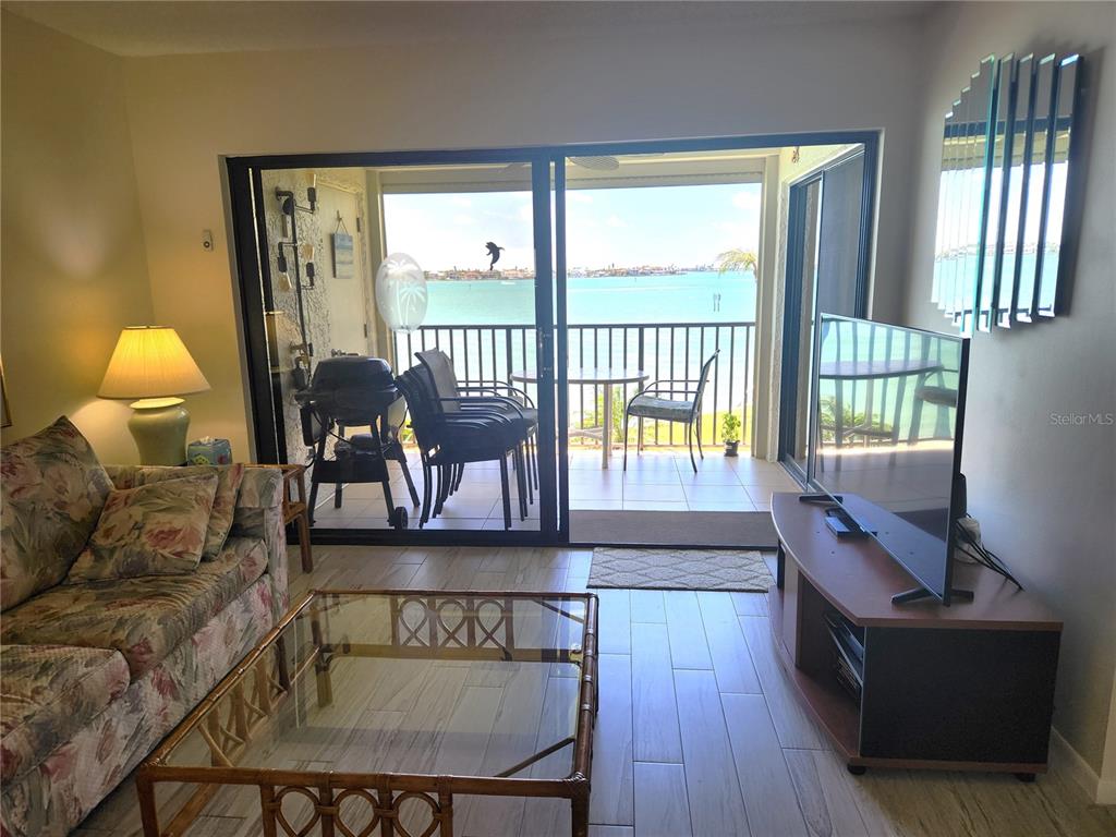 A living room features a floral sofa, glass coffee table, television, and a balcony overlooking water — 6287 BAHIA DEL MAR CIRCLE UNIT 311, ST PETERSBURG, FL