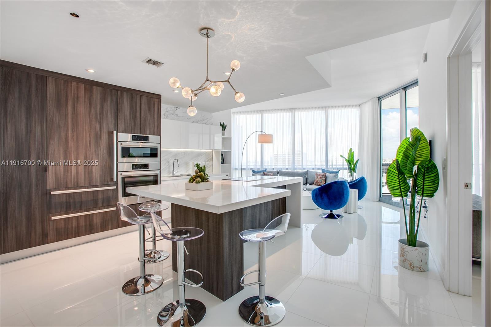 A modern kitchen features a white island, dark wood cabinetry, and blue accent chairs — 851 NE 1ST Ave # 1810, Miami FL 33132, MIAMI, FL