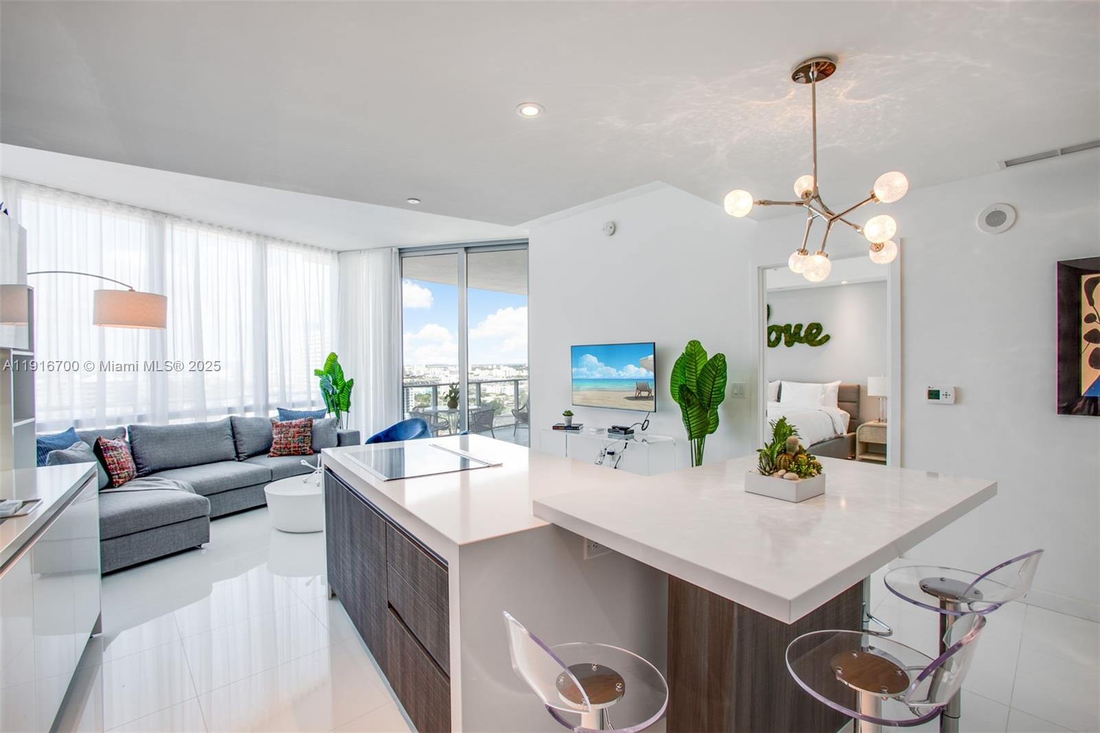 A modern open-concept living area features a kitchen island, gray sectional sofa, and floor-to-ceiling windows — 851 NE 1ST Ave # 1810, Miami FL 33132, MIAMI, FL