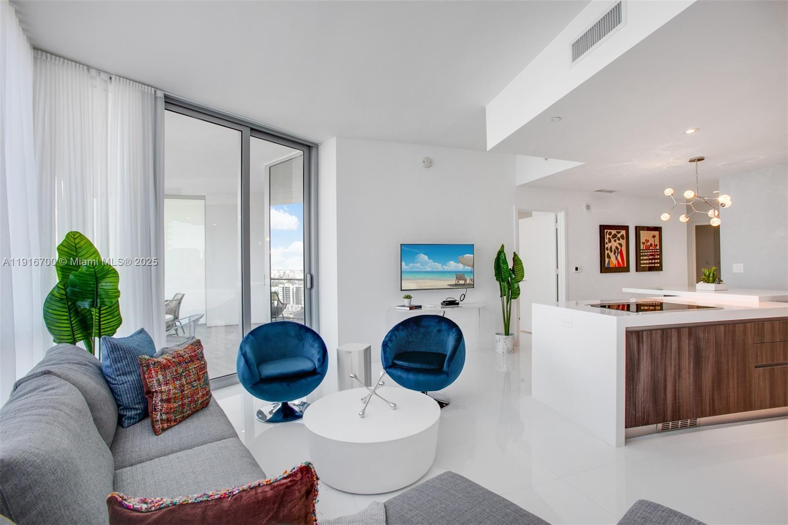 A modern living room features white floors, blue velvet chairs, and an open kitchen island — 851 NE 1ST Ave # 1810, Miami FL 33132, MIAMI, FL