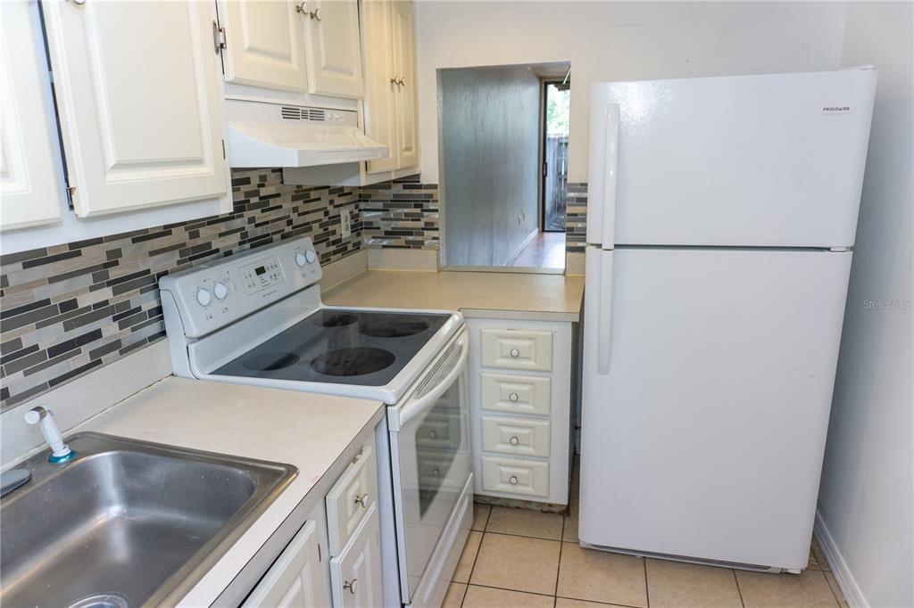 A kitchen features white cabinets, a glass-top stove, a refrigerator, and a tiled backsplash — 603 SW 75TH STREET UNIT 104, GAINESVILLE, FL