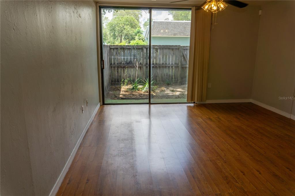 A room with wood-look flooring and a sliding glass door leading to a fenced patio — 603 SW 75TH STREET UNIT 104, GAINESVILLE, FL