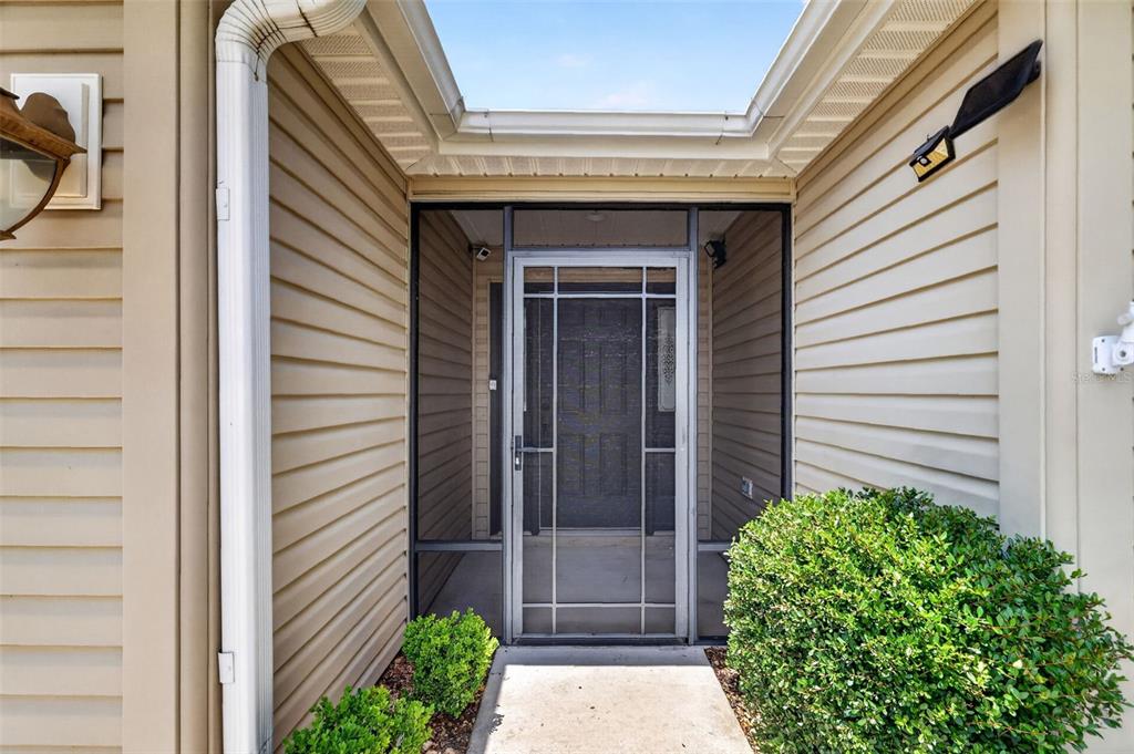 A front entryway features a screened door, beige siding, and a small concrete walkway — 791 ENISGROVE WAY, THE VILLAGES, FL