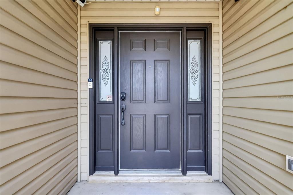A dark-colored front door with sidelights is framed by light-colored horizontal vinyl siding — 791 ENISGROVE WAY, THE VILLAGES, FL