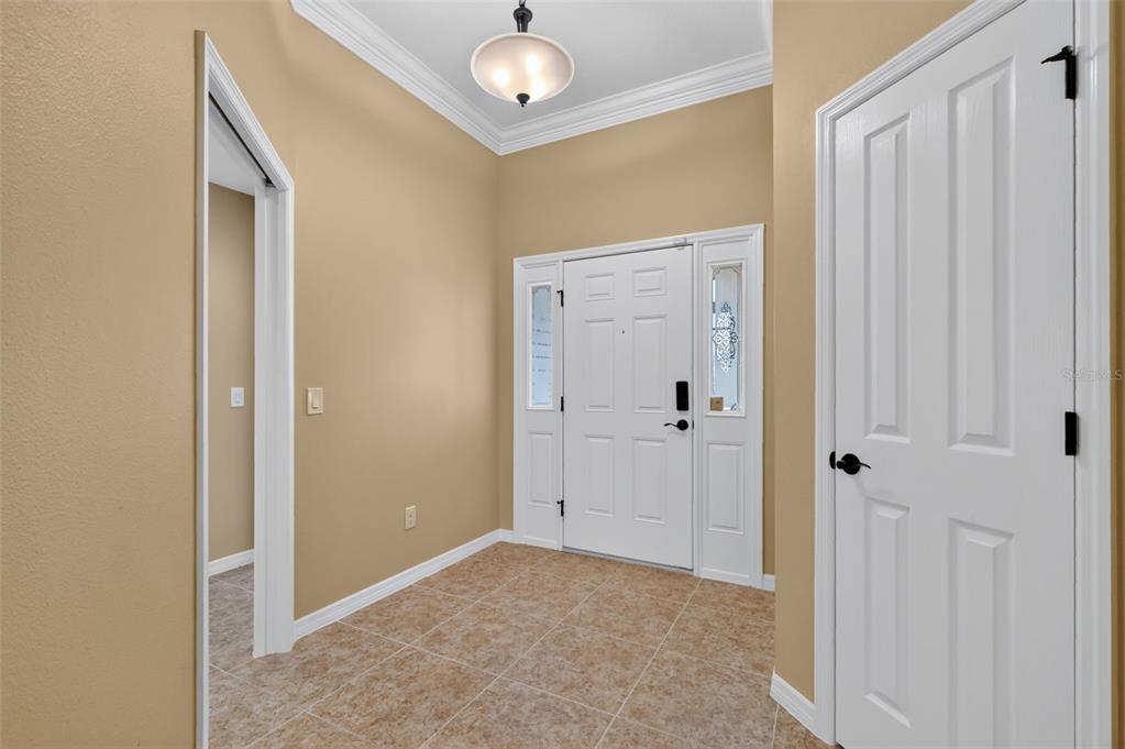An entryway features tan walls, tile flooring, a white front door, and a ceiling light — 791 ENISGROVE WAY, THE VILLAGES, FL