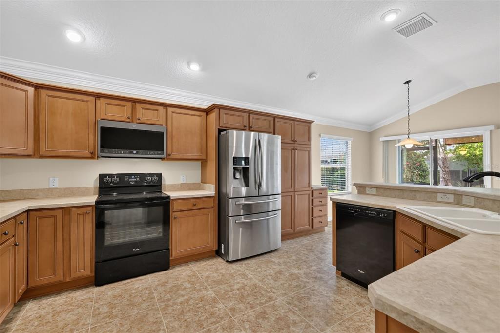 A kitchen features wood cabinets, stainless steel appliances, a black dishwasher, and tile flooring — 791 ENISGROVE WAY, THE VILLAGES, FL