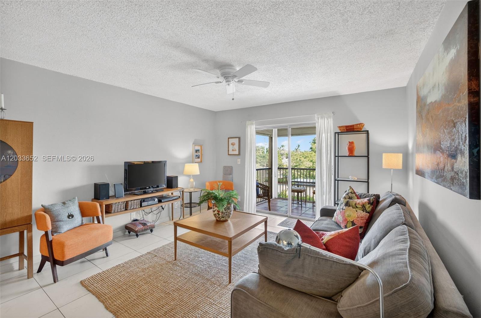 A living room features a gray sofa, orange accent chair, coffee table, and sliding glass doors — 257 S Cypress Rd # 436, Pompano Beach FL 33060, POMPANO BEACH, FL