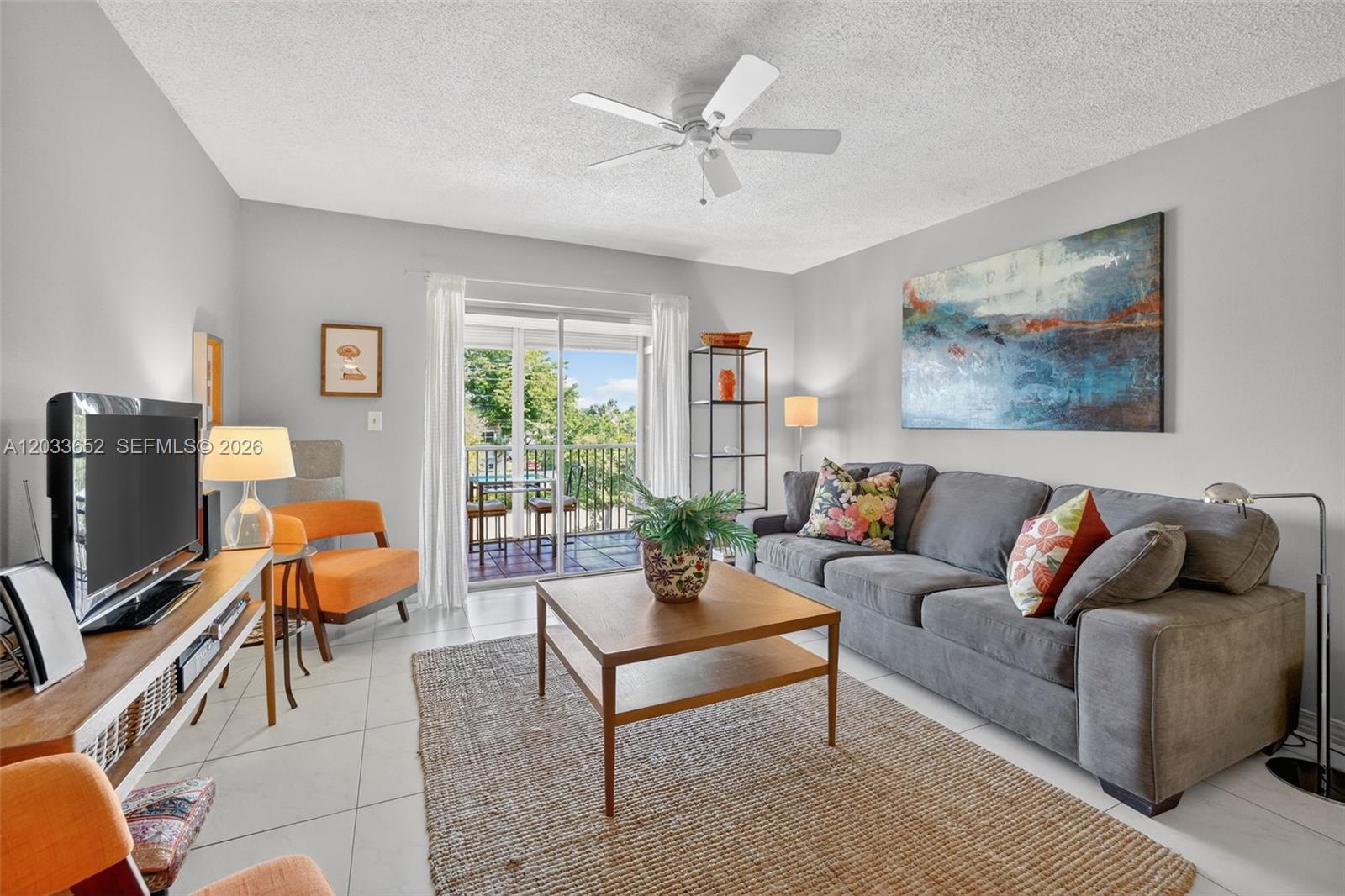 A living room features a gray sofa, orange chairs, a coffee table, and a balcony — 257 S Cypress Rd # 436, Pompano Beach FL 33060, POMPANO BEACH, FL