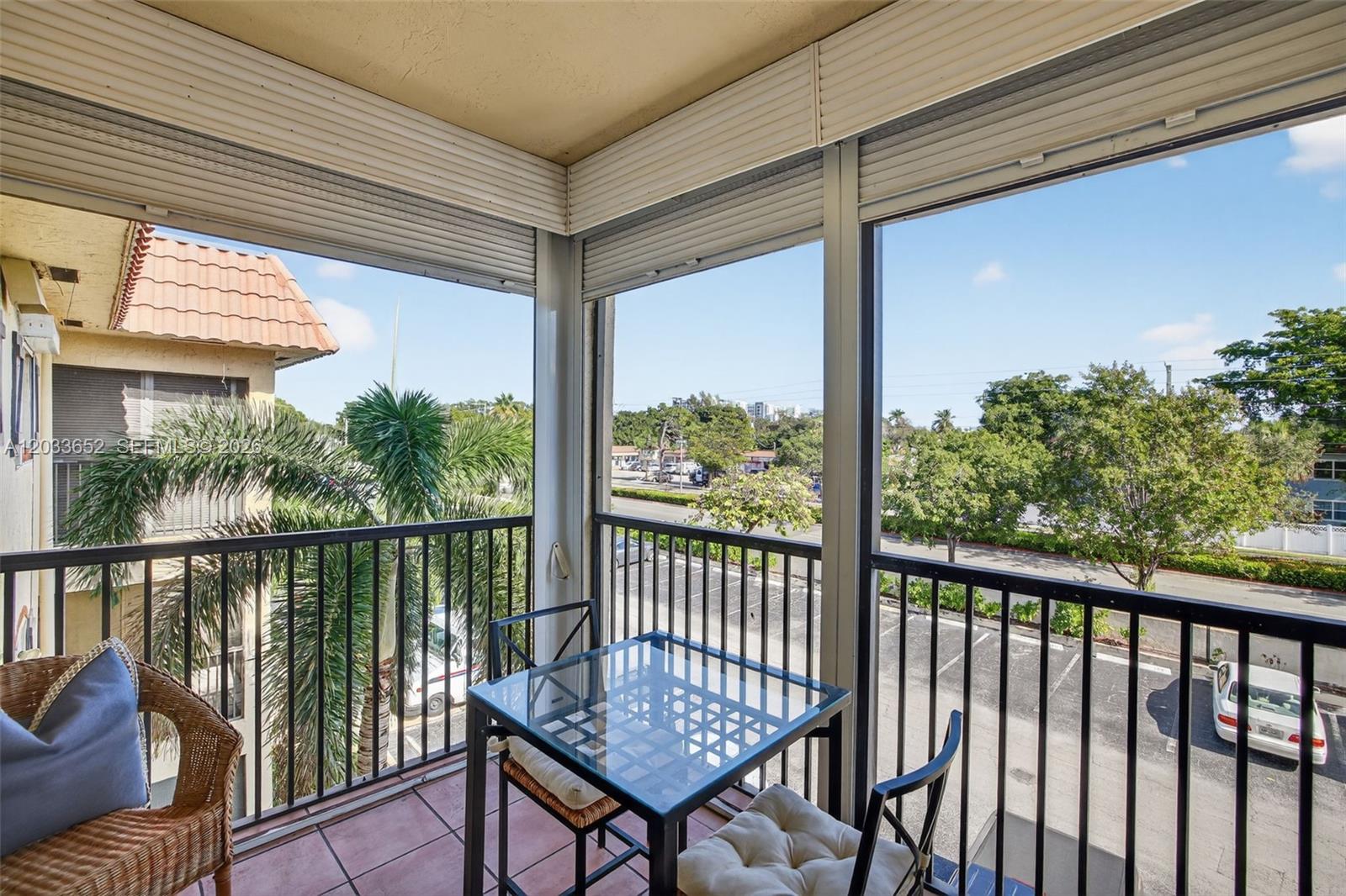 A balcony with a glass-topped table, chairs, and a view of a parking lot — 257 S Cypress Rd # 436, Pompano Beach FL 33060, POMPANO BEACH, FL