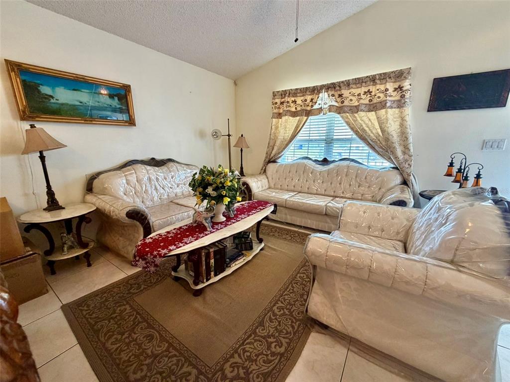 A living room features white tufted sofas covered in plastic, a coffee table, and curtains — 2319 LILY PAD LANE, KISSIMMEE, FL