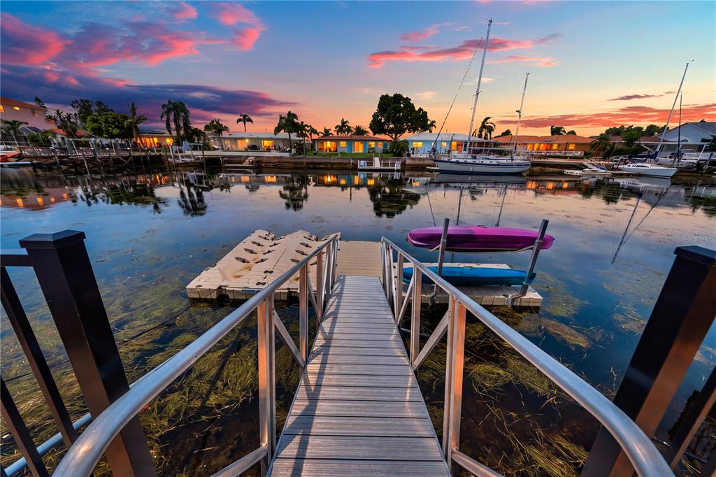 A metal walkway leads to a floating dock with two kayaks on a calm canal — 5004 ENSIGN LOOP, NEW PORT RICHEY, FL