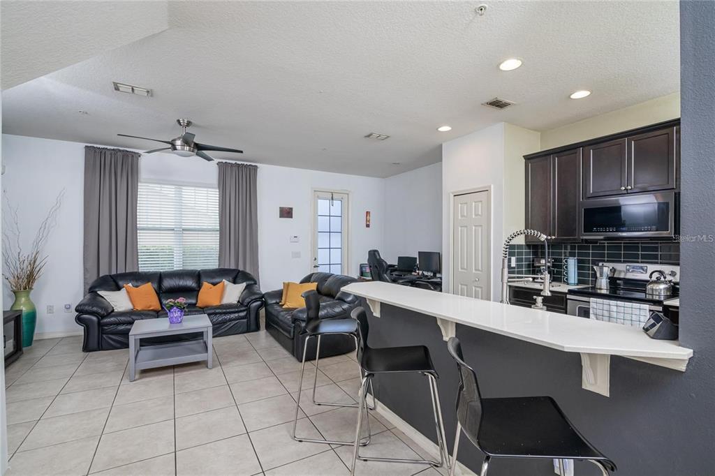An open-concept living room and kitchen featuring dark leather sofas, tile flooring, and a breakfast bar — 10184 HARTFORD MAROON ROAD, ORLANDO, FL