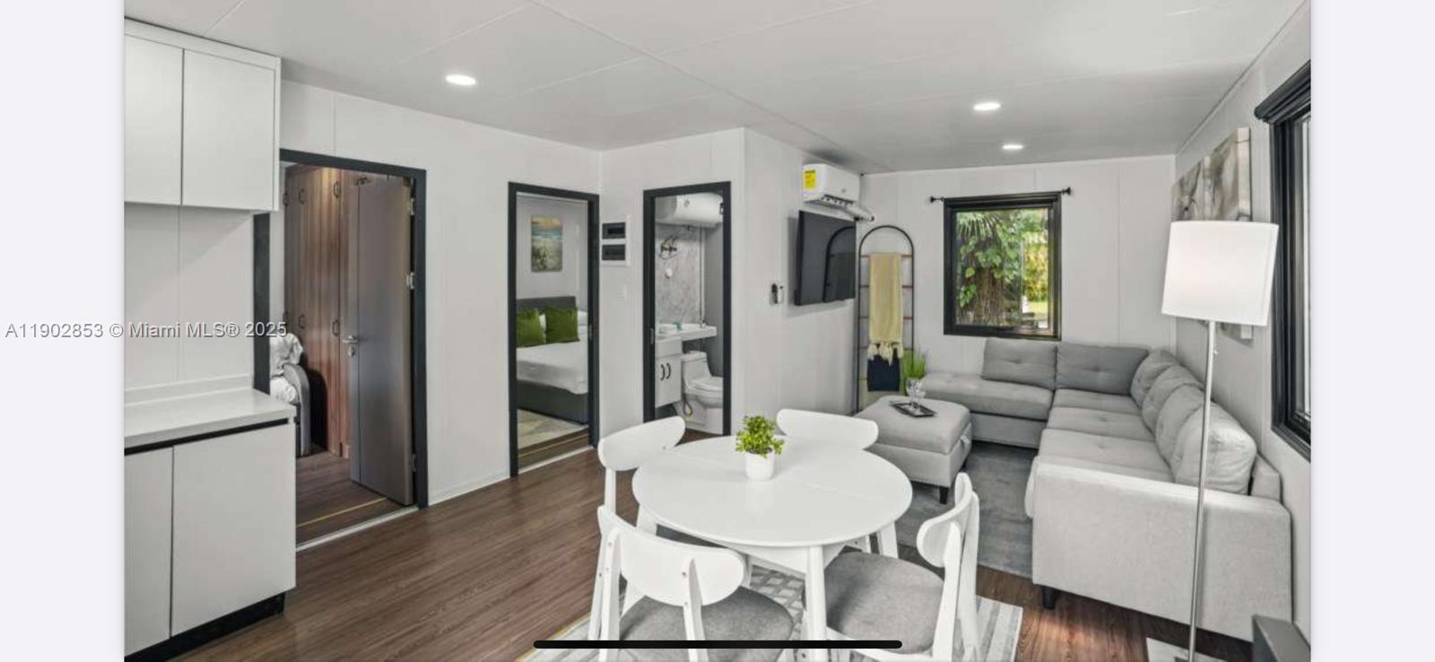 A modern open-concept living area features a white kitchen, dining table, and gray sectional sofa — 3460 70th Avenue NE, Naples FL 34120, NAPLES, FL