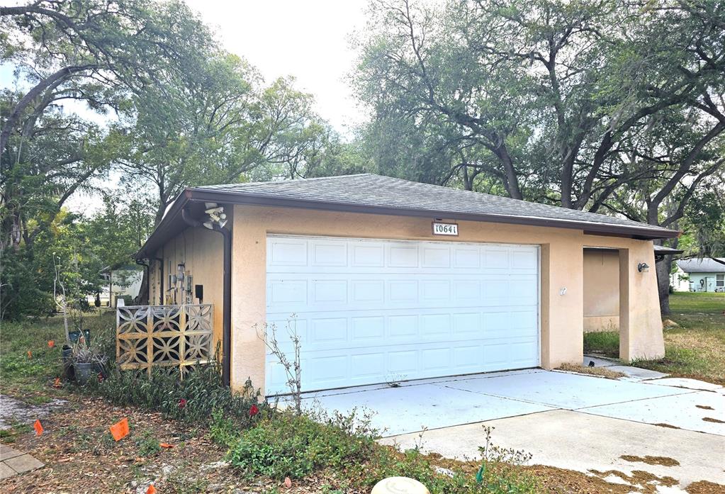 A detached garage with a white sectional door and a beige stucco exterior — 10641 TIMBER LANE, PORT RICHEY, FL