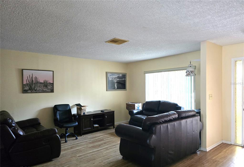 A living room features light-colored walls, wood-look flooring, two dark leather sofas, and a television console — 10641 TIMBER LANE, PORT RICHEY, FL